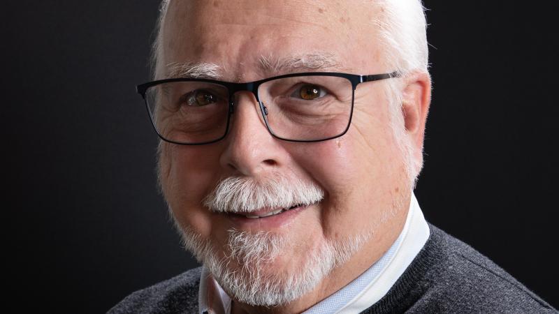 A male with white hair, beard and glasses