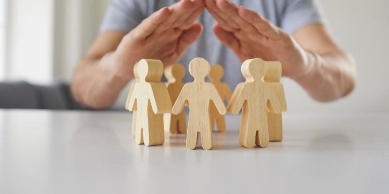 Wooden people figures in a circle with human hands protecting them