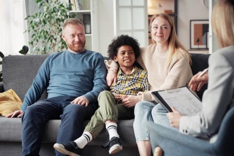 Two adults surrounding a child seated on a couch who are talking with a therapist