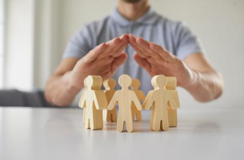 Wooden people figures in a circle with human hands protecting them